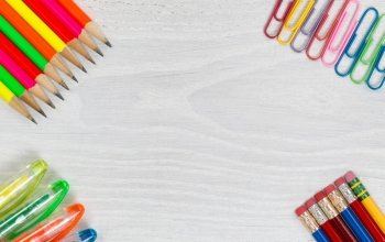 Bright colorful pencils, pens and paper clips on all white wooden desktop corners. High angled view in horizontal format.