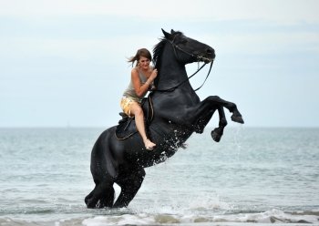 young woman and her beautiful black stallion rearing up in the sea