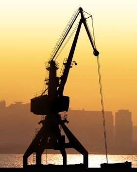 crane sit dramatically against a colorful sunset in a large shipyard