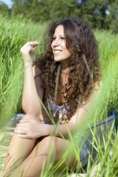 happy beautiful brunette young woman sits in green grass