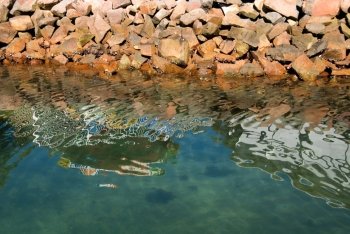 Reflections in the water near a man-made rock breakwater