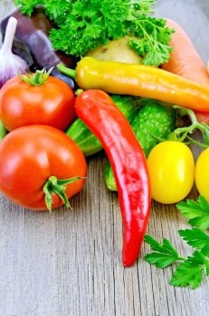 Red and yellow tomatoes, sweet and hot peppers, cucumbers, potatoes, carrots and parsley on a wooden boards background