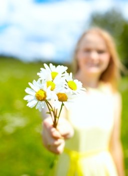 A young girl stretching out a bunch of camomiles. Shallow dof, focus is on the camomiles.