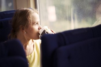 Pensive blond young woman drinking coffee and looking out the window while traveling by train