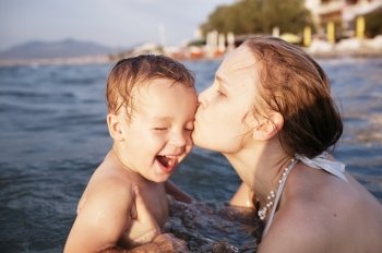 Mother kissing her young child while bathing in the sea waters during sunset