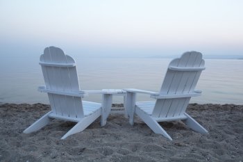 Empty white painted wooden deck chairs on a beach overlooking a calm ocean