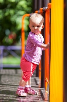Small infant holding on to rail standing in the playground