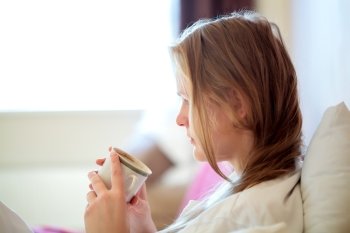 Candid side view portrait of a young blond woman drinking coffee sitting looking down at the mug in her hands, with copyspace