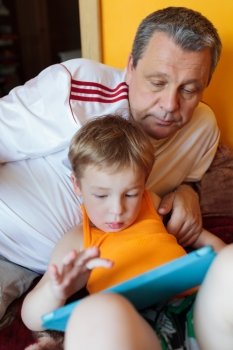 Grandfather watching grandson playing on the tablet PC