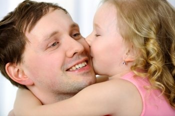 Close-up shot of a little daughter hugging and kissing father. Touching love of child to parent. Little girl kissing fathers cheek