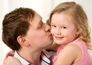 Close-up shot of young father kissing little smiling daughter. Sincere parents love. Daddy kissing beautiful little daughter