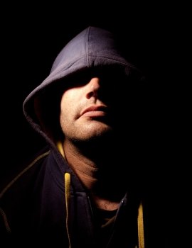 Portrait of a man with a cowl covering his eyes. Studio lighting. Half face illuminated, half face in shadows. 