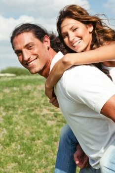 Smiling couple facing camera as man carries young lady on his back