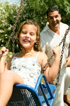 Young girl enjoying swing ride with father in background