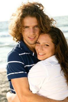 Young guy and lady smiling at camera while hugging on the beach
