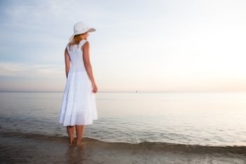 Woman in hat and white dress on the beach 