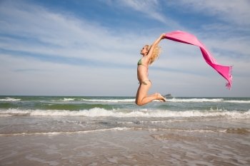 Happy beautiful woman jumping with pink shawl on the beach