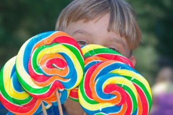 young boy looks over the top of four huge lollipops. boy with lollipops