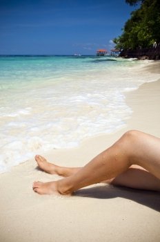 Womans legs on beautiful tropical beach with bright sand