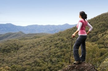 Single female hiker looks out at view in mountains with forest below her