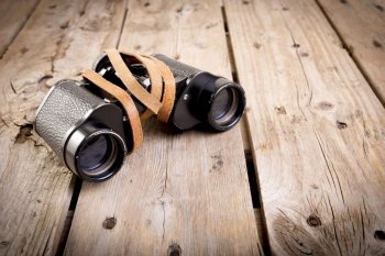 Pair of old binoculars with vintage leather strap on a rough wooden surface