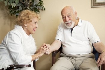 Senior couple in the waiting room of the doctor’s office holding hands for moral support.