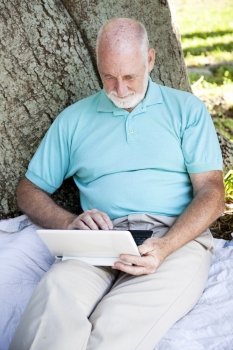 Senior man using his wireless netbook computer outdoors.  