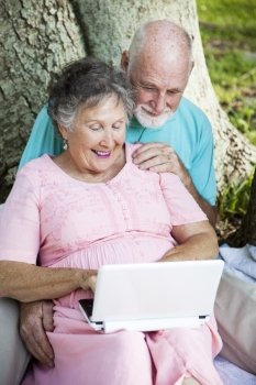 Senior couple has fun using a netbook computer in the park.  