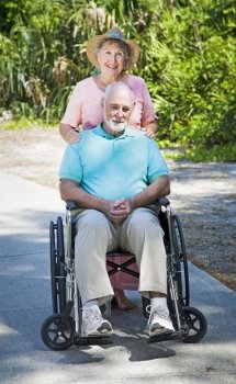 Senior lady pushing her husband in his wheelchair.  