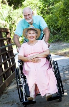 Senior man pushing his disabled wife through the park in a wheelchair.  