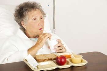Senior woman in the hospital, eating lunch and drinking from a straw.  