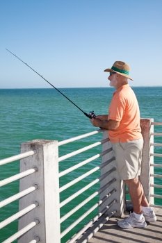 Retired senior man enjoys fishing from a pier into the ocean.  