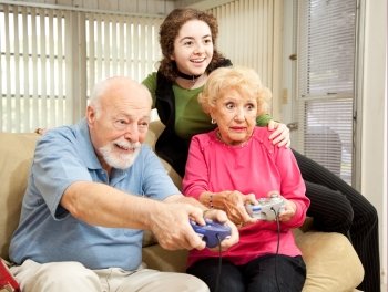 Senior man and woman play video games while their granddaughter looks on.  