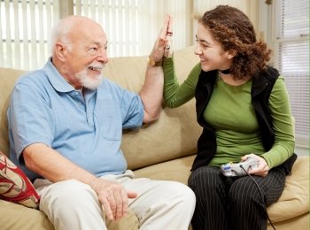 Teen girl playing video games, getting a high five from her grandfather.