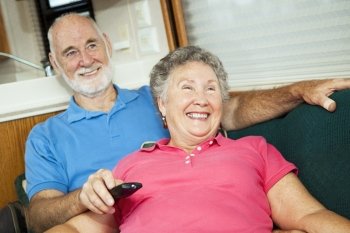Happy senior couple laughing as they watch TV together in their motor home.  