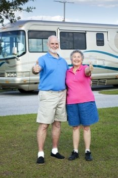 Senior couple in front of their luxury RV, giving thumbs up sign.  
