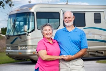Active retired couple in love with their luxury motor home in background.