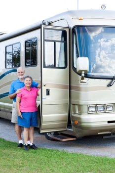 Happy retired couple standing beside their luxury motor home.  