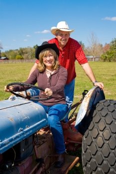 Mature married couple riding the tractor on their farm.  