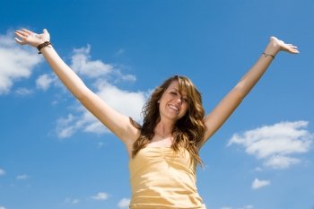 Beautiful teen girl raising her hands in joy and praise against a blue sky.