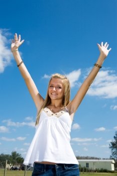 Beautiful blond teen girl outdoors raising her arms in freedom.  