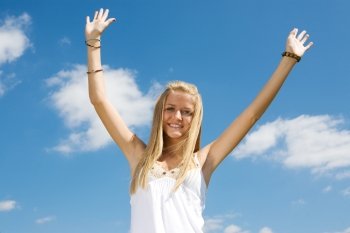 Enthusiastic young teen girl raising her arms in celebration against a blue sky.  