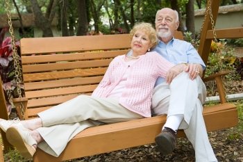 Senior couple taking time to relax together on a park swing.  