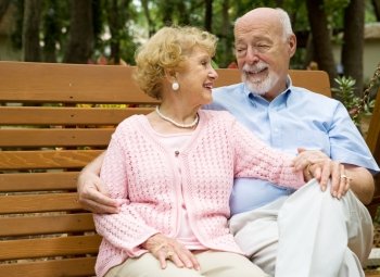 Happy senior couple relaxes together on a park bench.  