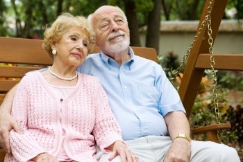 Attractive senior couple relaxing together on a swing in the park.  