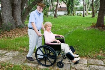 Disabled senior woman being pushed through the park in a wheelchair by her loving husband.  