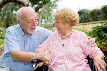 Senior couple talking and laughing together outdoors.  She is in a wheelchair.  