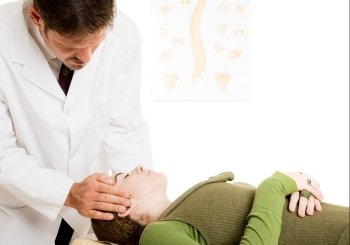 Chiropractor gently adjusting a patient’s neck in his office.  