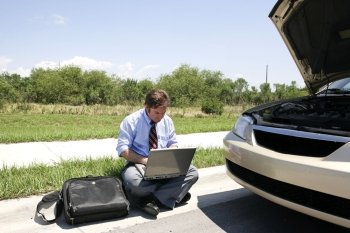 A businessman working in the sun by the side of his broken down car.  