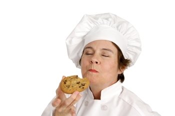 Chef enjoying a delicious chocolate chip cookie she just baked.  Isolated on white.